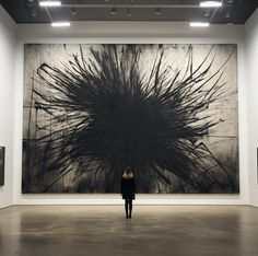 a woman standing in front of a large painting on display at an art gallery with black and white artwork