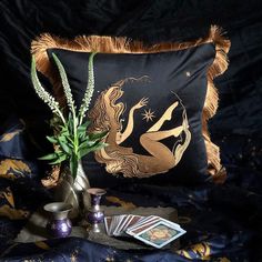 a decorative pillow and some cards are on a bed with a black blanket, two vases and a card game