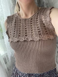 a woman standing in front of a window wearing a brown top with crochet