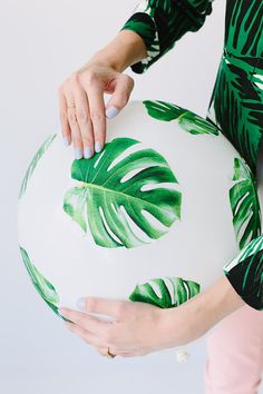 a woman holding a large white ball with green leaves painted on it and her hands