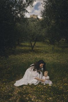 a mother and her child sitting in the grass under an apple tree with ruins in the background