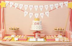 a birthday cake and cupcakes are displayed on a table in front of a pink wall