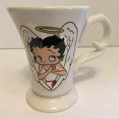 a cup with an angel on it sitting on a table next to a white wall