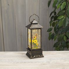 an old fashioned lantern with yellow flowers on the inside is sitting on a wooden table