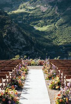 an outdoor ceremony setup with wooden chairs and flowers on the aisle, overlooking mountains in the distance