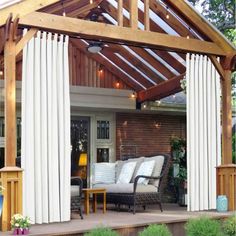 an outdoor covered patio with blue curtains on the side and furniture in the back yard