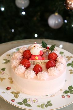 a white cake topped with strawberries on top of a plate next to a christmas tree