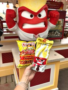 a person holding up a bag of chips in front of a red and white mascot