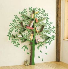 a green tree with books on it in front of a white wall and wooden floor