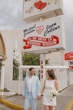 a man and woman holding hands walking in front of a sign for a wedding venue