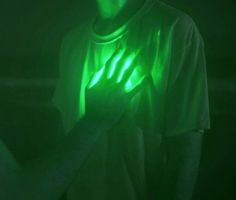 a man holding his hands up in the dark with green light shining on him from behind