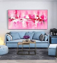 a living room with blue couches and pink painting on the wall above it's coffee table