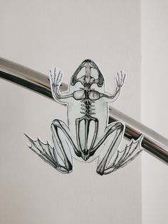 a glass frog sitting on top of a metal bar next to a white wall and floor