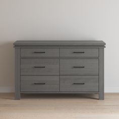 a gray dresser sitting on top of a hard wood floor next to a white wall