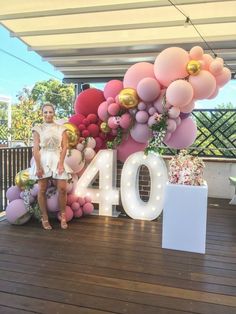 a woman standing in front of a large number sign with balloons and flowers on it