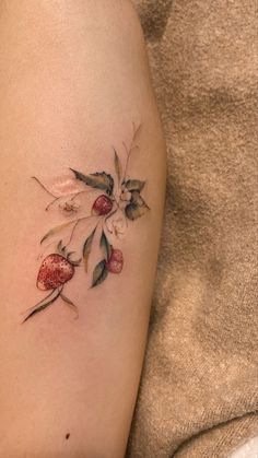 a small tattoo on the arm of a woman with strawberries and leaves growing out of it