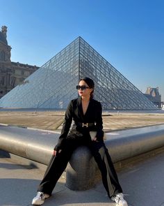 a woman sitting on top of a cement pillar next to a large pyramid in the background