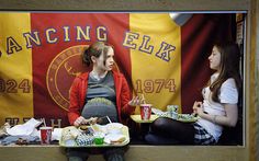 a pregnant woman sitting in front of a table with food on it and two sodas