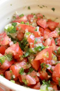 a white bowl filled with chopped tomatoes and cilantro on top of a table