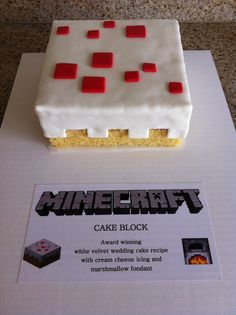 a white cake with red squares on it sitting on top of a table next to a sign that says minecraft