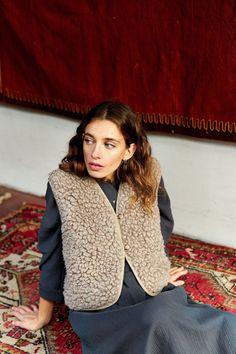 a woman is sitting on the floor in front of a rug and wearing a vest