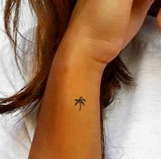 a woman with a small palm tree tattoo on her left wrist and right hand behind her ear