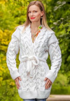 a woman wearing a white sweater and jeans standing in front of trees with her hands on her hips