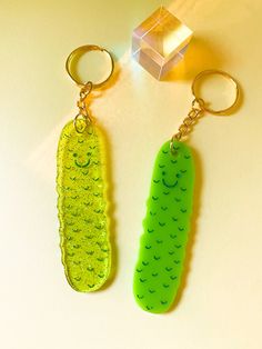 two keychains made to look like peas on a white surface with a cube in the background