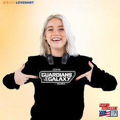 a woman with white hair wearing headphones and holding up a black shirt that says guardians the galaxy