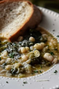 a white plate topped with beans and greens next to a slice of bread on top of it