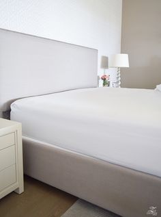 a white bed sitting next to a night stand with a lamp on top of it