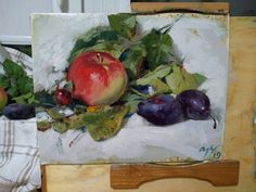 an apple, plums and leaves are displayed on a easel next to another painting