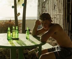 a shirtless man sitting at a table with beer bottles in front of his face