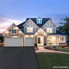 a large house with two garages and lights on it's front porch at dusk