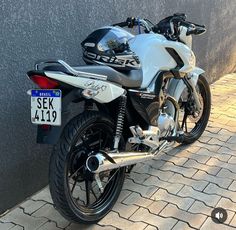 the motorcycle is parked on the side of the road next to a wall with a number plate