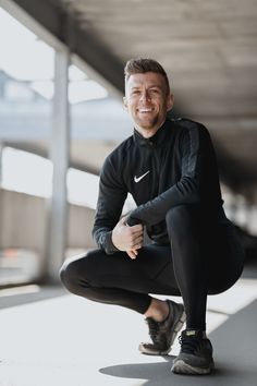 a man sitting on the ground with his legs crossed and smiling at the camera while wearing black