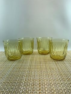 four yellow glass cups sitting on top of a woven tablecloth covered floor next to each other