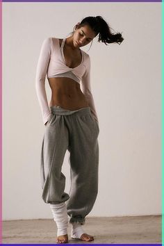 a woman standing in front of a white wall wearing grey sweatpants and a pink crop top