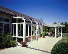 a white house with lots of windows and plants in the front garden area, along with a pergolated patio