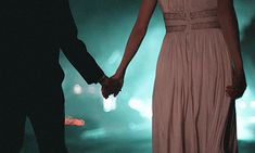 a man and woman holding hands while standing next to each other in front of bright lights