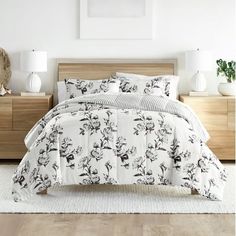 a white bed with black and white flowers on the comforter, next to two nightstands