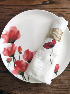 a white plate topped with a napkin covered in red flowers and a roll of gold wire