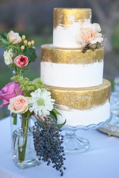 a white and gold wedding cake sitting on top of a table next to some flowers