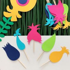 colorful paper cutouts on sticks with grass in the backgroung area behind them