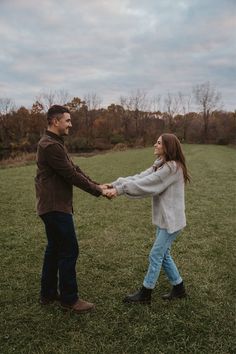 a man and woman holding hands while standing in the middle of a grassy field on a cloudy day