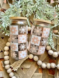 two vases with flowers on them are sitting next to some beads and greenery