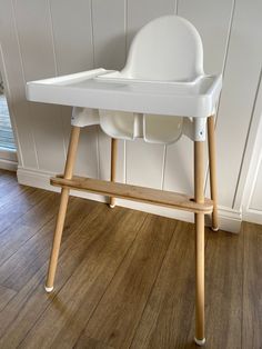 a white high chair sitting on top of a hard wood floor next to a wall