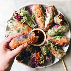 a person dipping sauce onto some food on a white plate with chopsticks in it