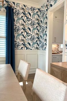 a dining room table with white chairs and blue wallpaper