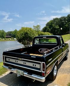 an old black truck parked on the side of a road next to a body of water